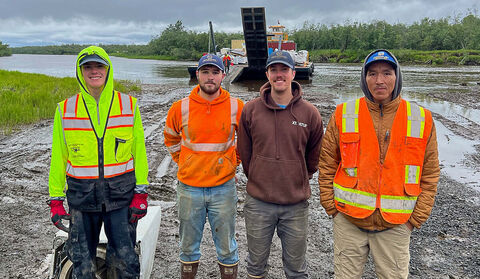 Four young men standing in front of a river barge in Southwest Alaska.