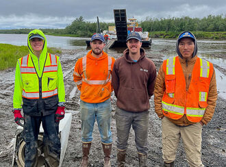 Four young men standing in front of a river barge in Southwest Alaska.