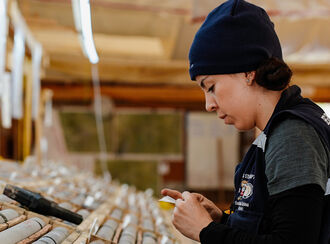 A female geologist logs core inside a building at the Lawyers-Ranch project.