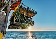 A tracked mining machine being lowered into the ocean at sunrise.