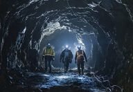 Three miners with headlamps approach an underground gold mine.