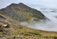 A drill rig sits above the clouds on a treeless mountain ridge in Alaska.