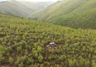 A rolling green landscape with a single lone drill rig set on the hillside.