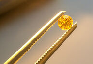 A pair of tweezers holding a fancy yellow diamond from the Naujaat project.