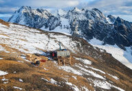 A drill tests for copper on an alpine slope in front of snow-dusted mountains.