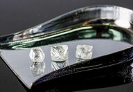 Three uncut raw diamonds placed on a shiny trowel.