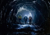 Three miners with hardhats and headlamps in an underground mine.