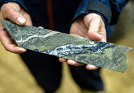 Hands hold half drill core cut diagonally by gold-rich quartz veins.