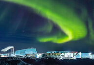 A ribbon of green aurora arcs above Meliadine Mine building lit up at night.