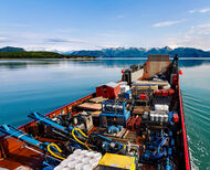 A barge loaded with supplies with Alaska mountains in the background.