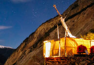 A canvas-enclosed drill rig glows yellow as it tests a KSM deposit at night.