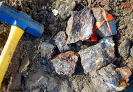 A sledgehammer lies alongside heavily mineralized rocks broken off an outcrop.