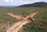 A cross shaped trench with an excavator in the middle of the Yukon wilderness.