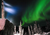 A band of green aurora behind a drill testing for gold during winter in Alaska.