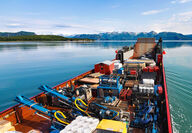 A barge loaded with mineral exploration equipment and supplies on calm waters.