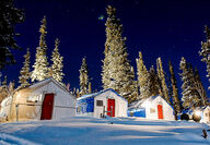 Lights from a tent camp illuminate the snowy landscape on a winter night.