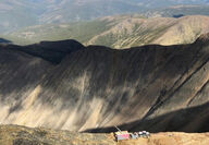 A lone drill rig along a ridge, with miles of mountains in the background.